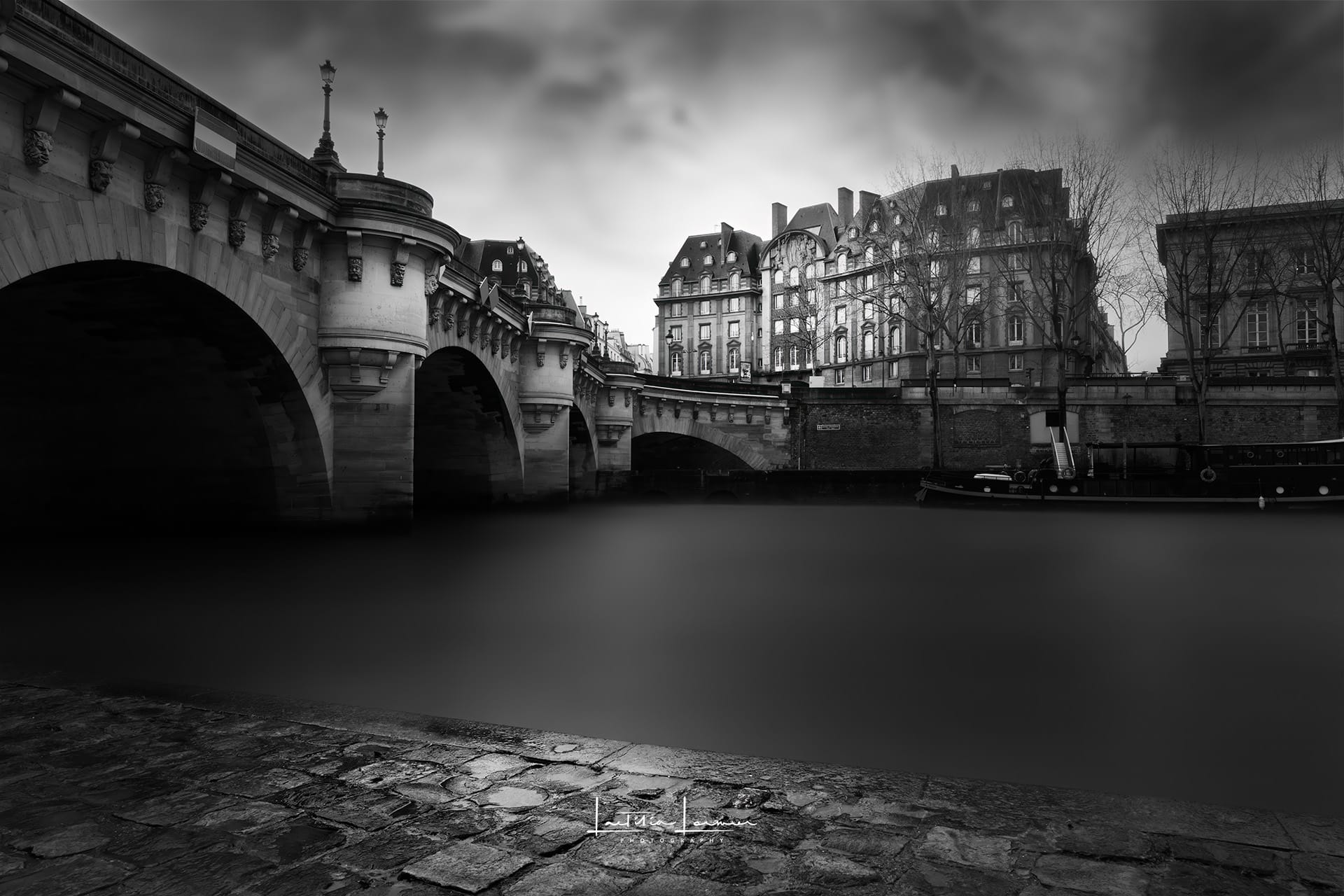 Photographie en noir et blanc du Pont Neuf avec la Seine en premier plan, capturée en pose longue pour un effet minimaliste et onirique.